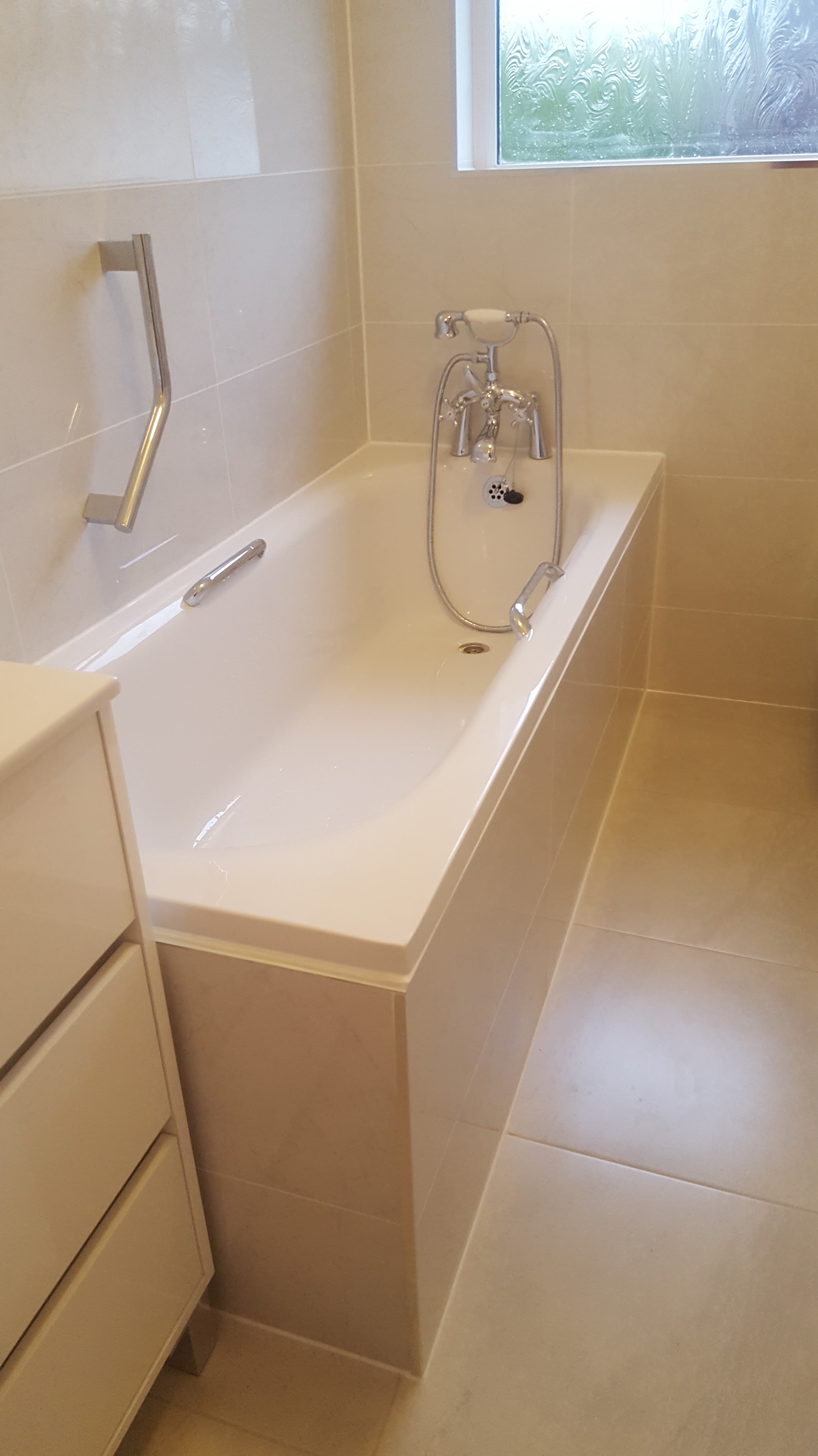Bath with a chrome grab rail and mixer, beside a cream vanity unit