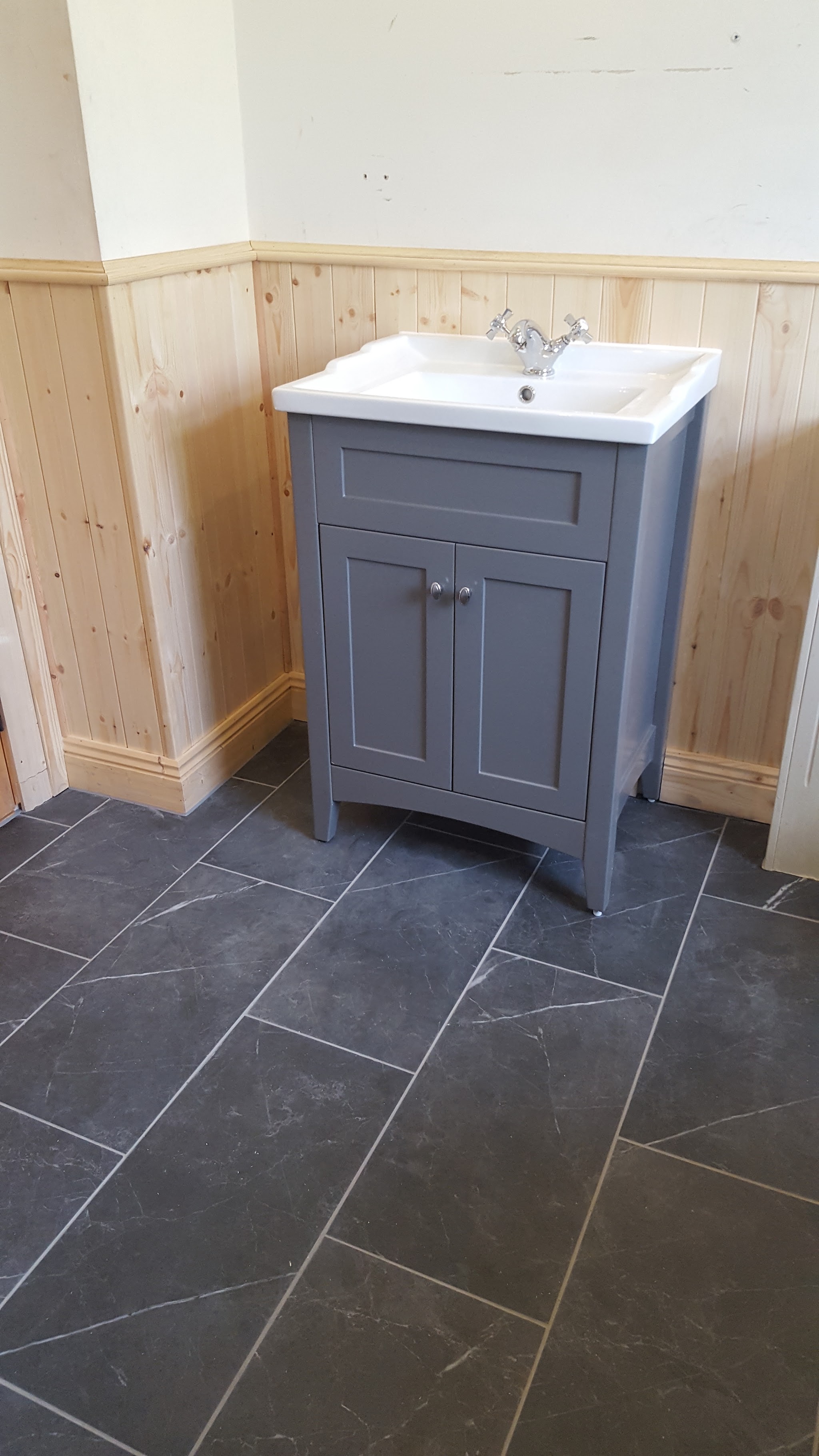 Grey freestanding vanity unit on a dark slate floor with timber panelling