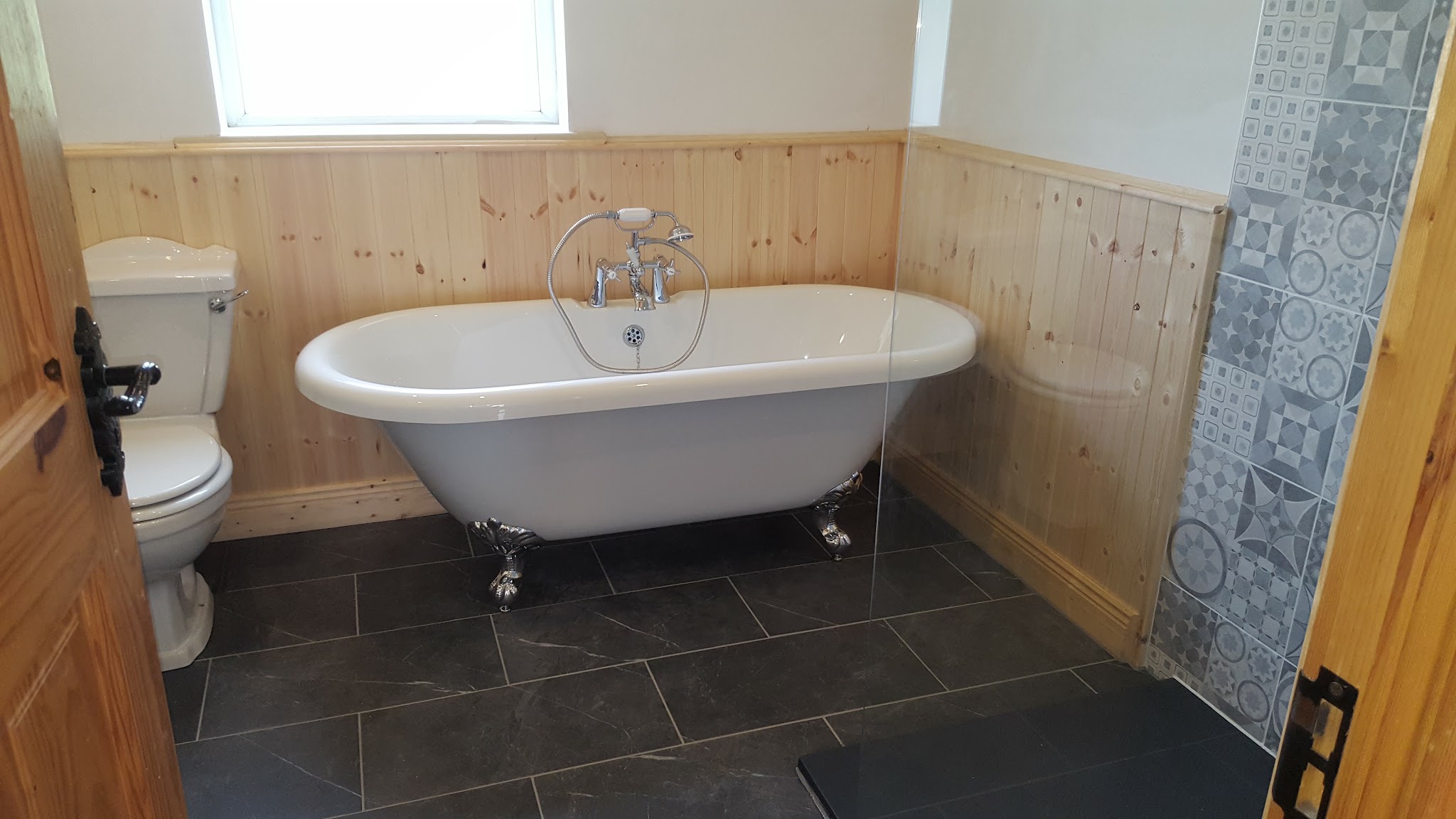Roll-top bath with timber wall panelling and patterned tiles