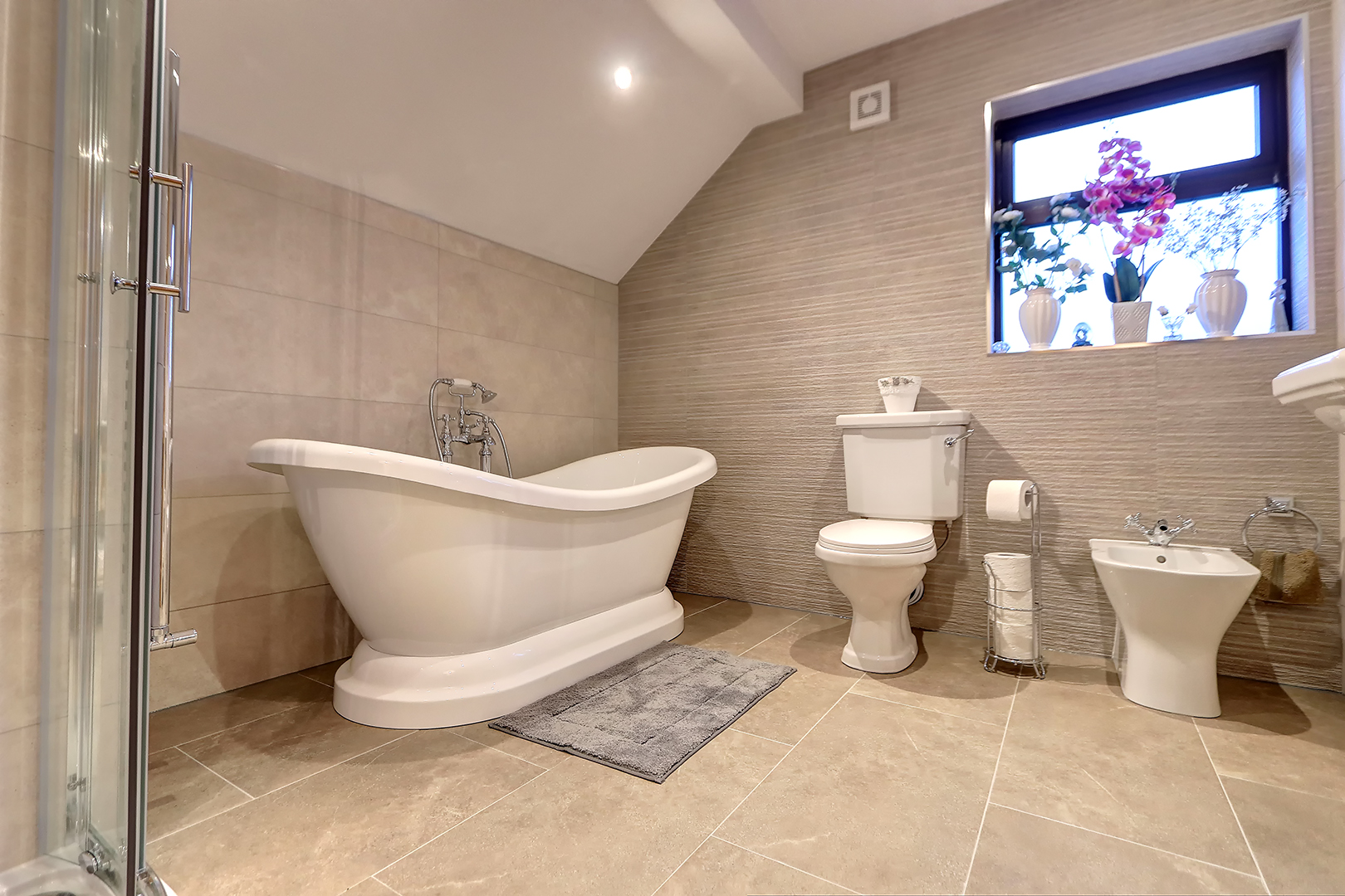 Finished attic bathroom with a freestanding slipper bath, toilet and bidet on large beige floor tiles