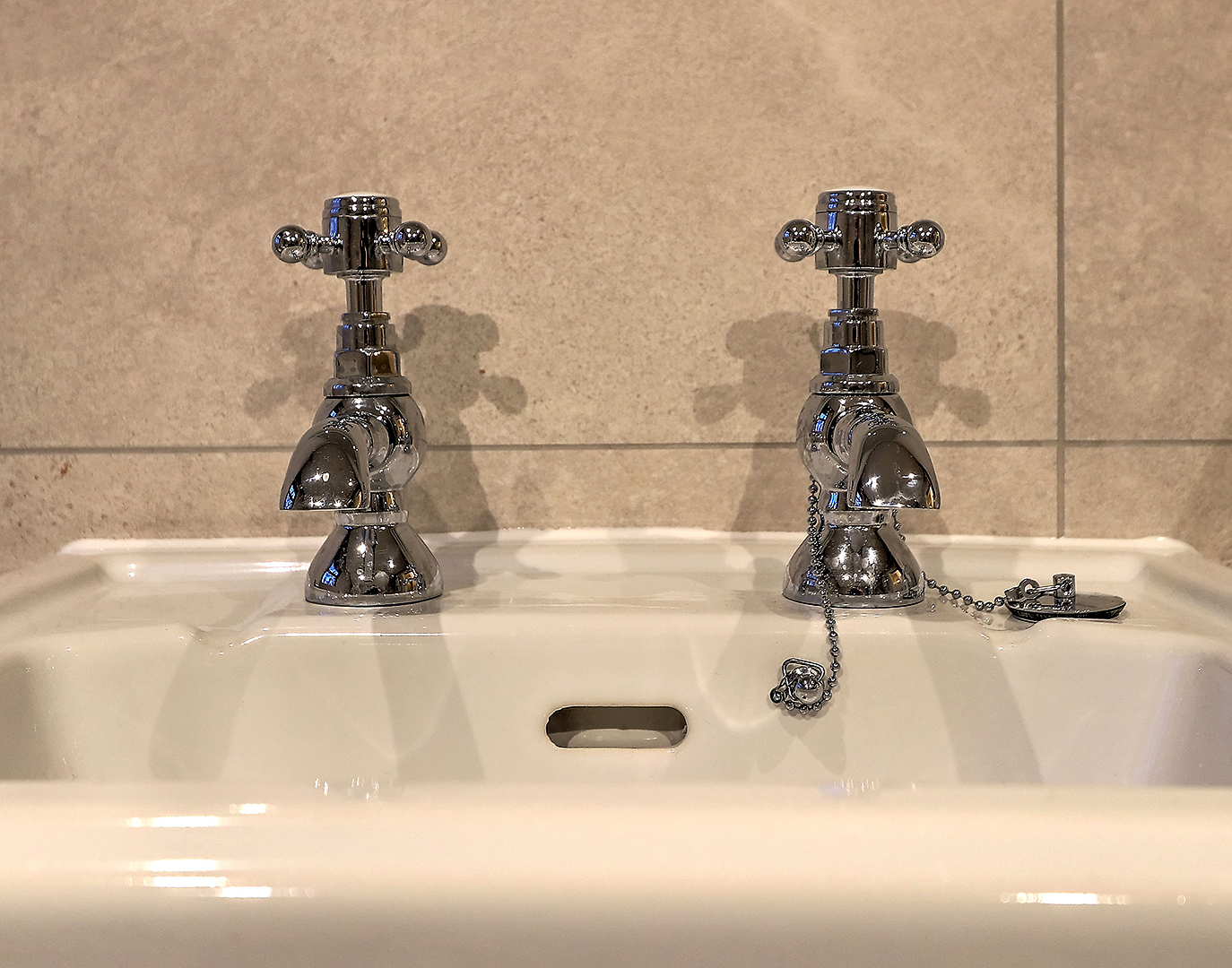 White basin with chrome cross-head taps against beige wall tiles